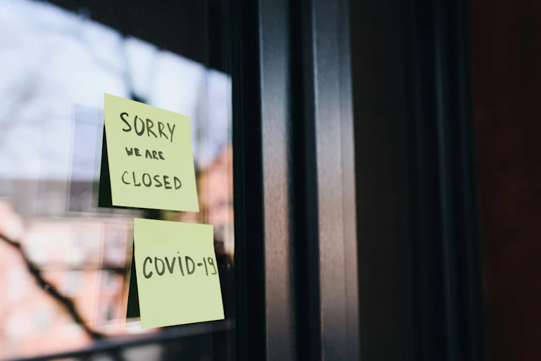 Two post-it notes on a window read SORRY WE ARE CLOSED and COVID-19.