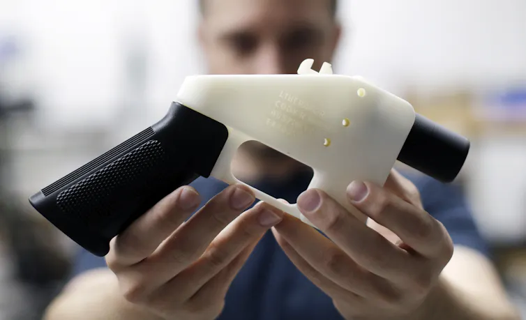 A man holds up a black and white plastic gun.