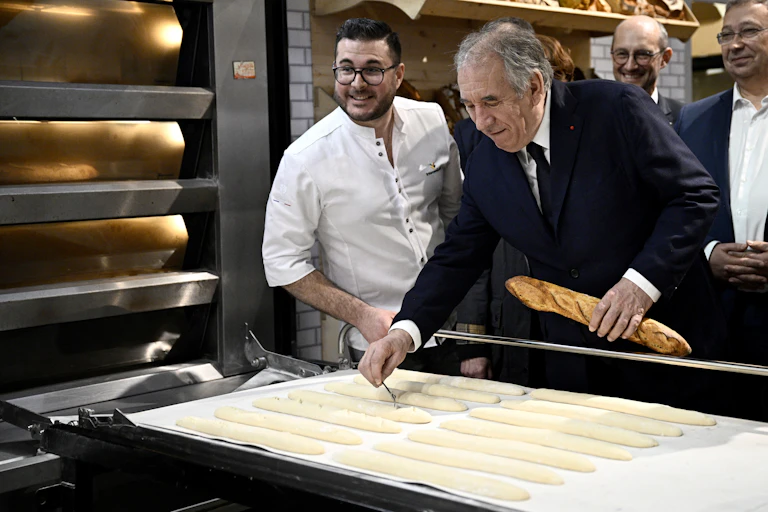 Image de François Bayrou qui prépare des pains dans une boulangerie avec une baguette à la main