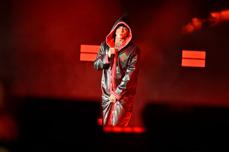 Rapper stood on stage holding a microphone, with his hood over his head.