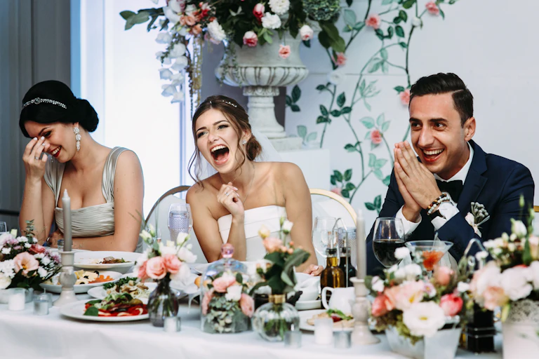 Bride, groom and bridesmaid laughing at a speech