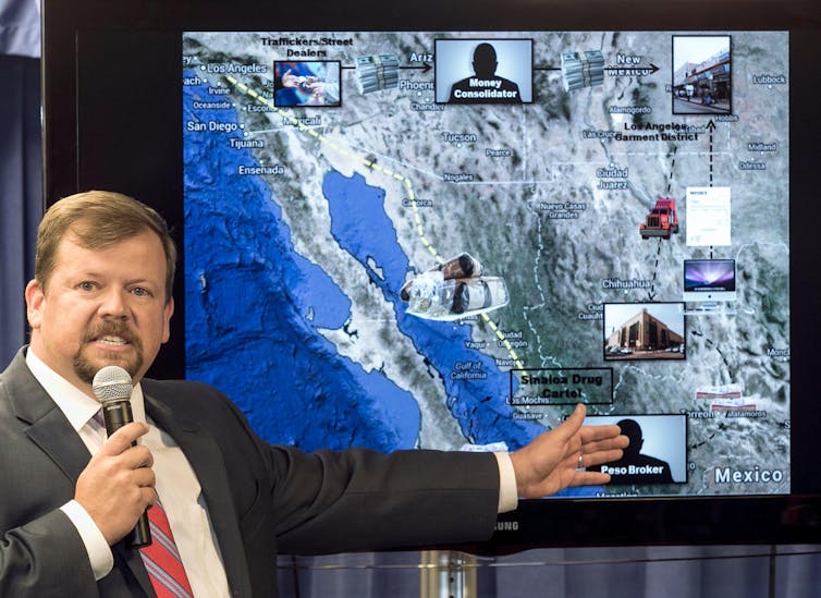 Bearded man with microphone stands in front of map of California.