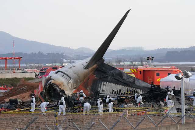 Rescue workers wearing white safety gear work through the wreckage of a burnt plane, which has crashed into the runway at a South Korean airport.