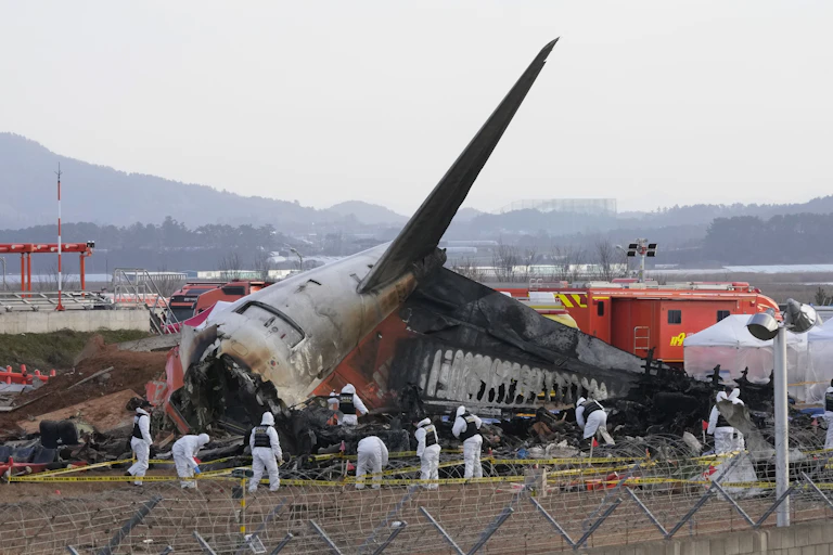 Rescue workers wearing white safety gear work through the wreckage of a burnt plane, which has crashed into the runway at a South Korean airport.