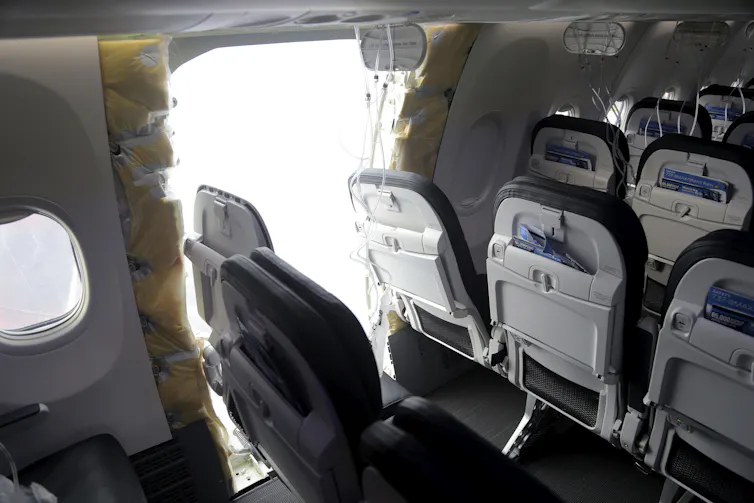 An airplane, with seats tilting towards a gaping hole where a door should have been.