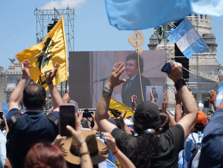 A crowd of people watch Javier Milei on a large screen.