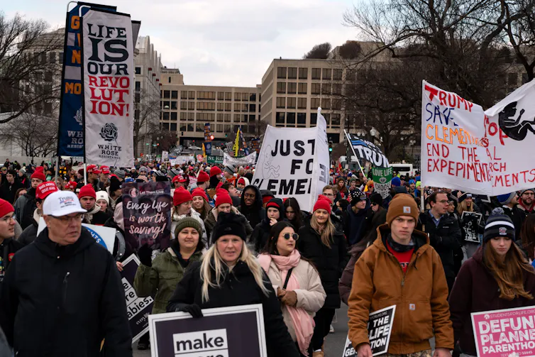 A large crowd marches while holding banners with various slogans. One such banner reads, 'Life is our Revolution.'