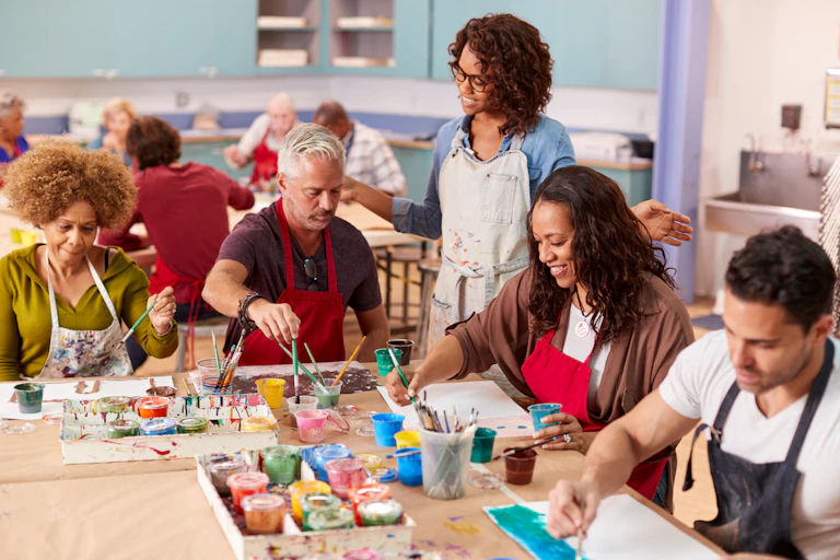 A group of adults paint on paper in a classroom.