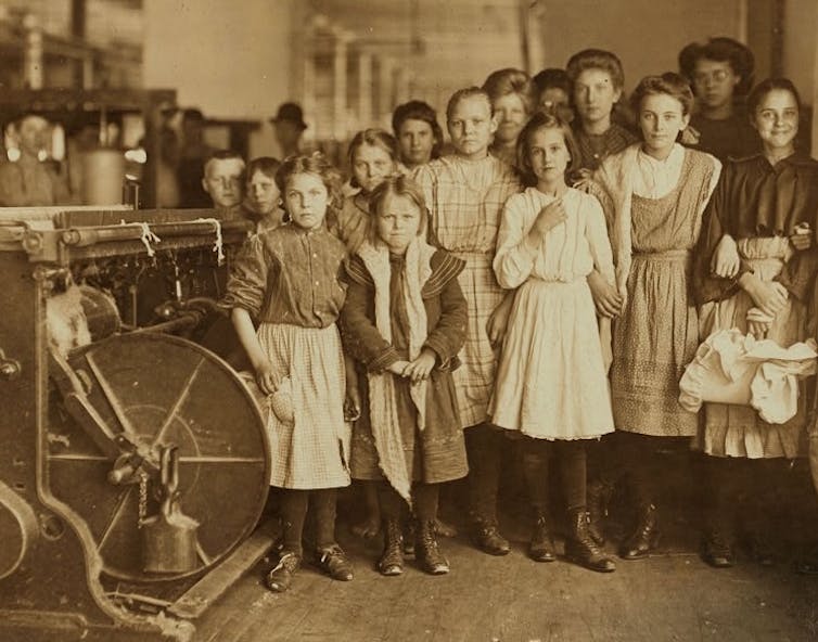 A group of girls and teenagers pose next to a cotton gin.