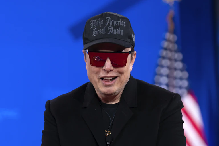a smiling man wearing a dark jacket over a T-shirt, dark ball cap and sunglasses