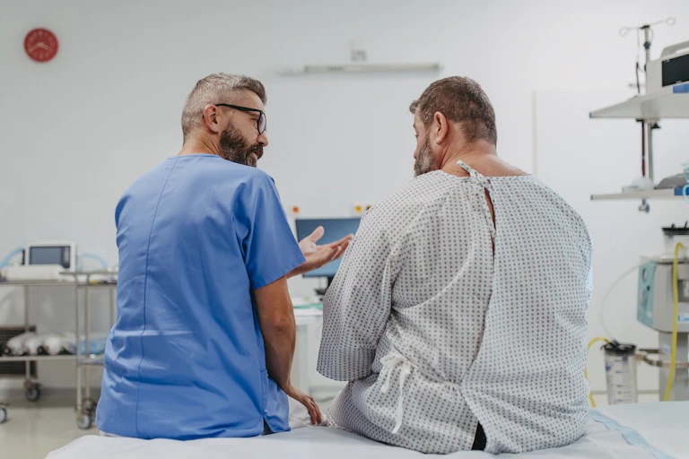 A doctor in blue scrubs sitting with an overweight man in a medical gown, seem from behind