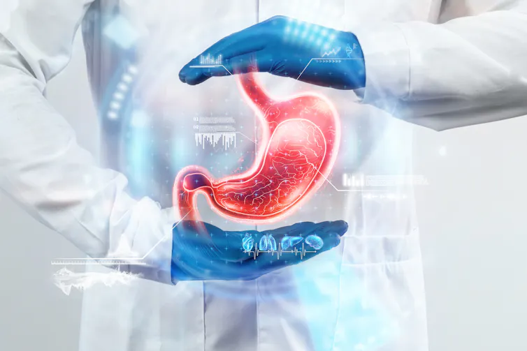 A person in a white coat out of frame wearing blue gloves framing a hologram of a stomach
