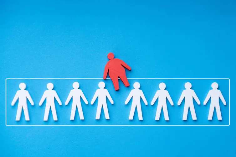 A line of white paper cutout human figures and one larger red figure being inserted into the line