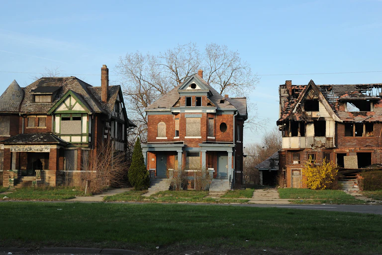 Three large houses with brick facades and interesting architectural detail are falling into ruin.