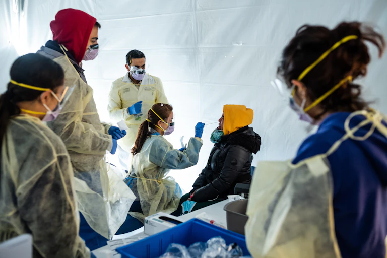 Inside a white tent, doctors wearing masks test a patient for COVID-19.