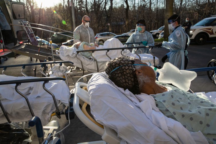 Medical staff members tend to patients on stretchers who are awaiting entrance to a hospital.