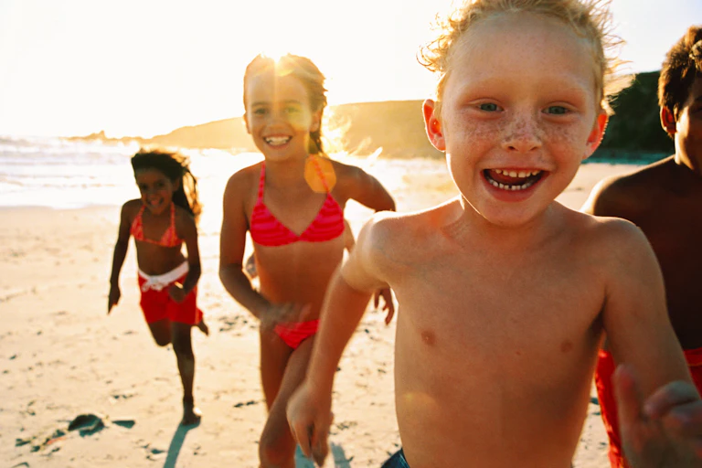 Smiling children in swim clothes on a beach, running toward the camera