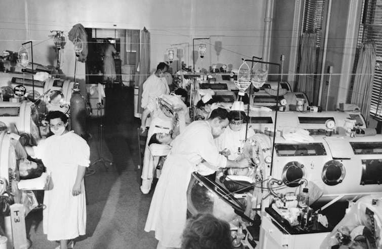 A historical photo of doctors and nurses treating polio patients in iron lung machines.