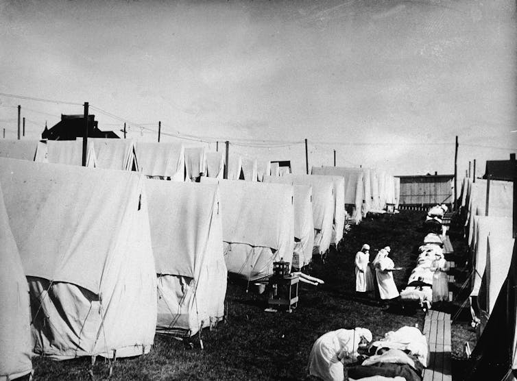 A historical photo of rows of white canvas tents and medical personnel working outside.