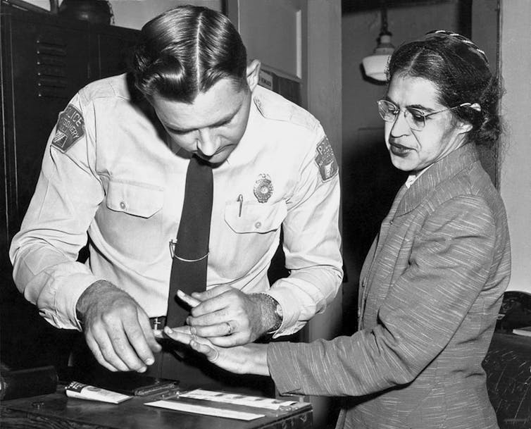 black and white photo of activist Rosa Parks being fingerprinted by police officer