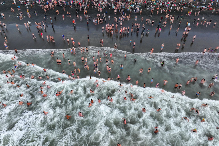 aerial view of hundreds of people on a beach and in the surf