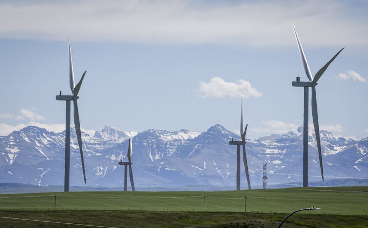 Turbinas eólicas vistas en un campo cubierto de hierba con una cadena de montaña en la distancia