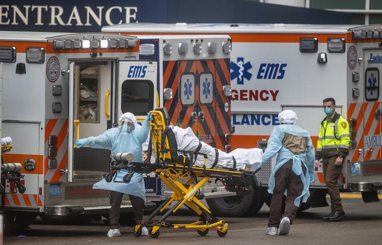 two EMTs in PPE rush a patient on a stretcher away from ambulance