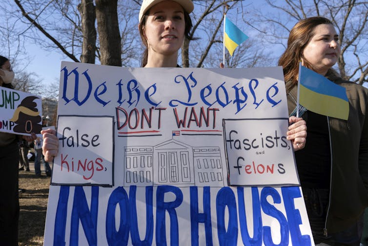 A person outside holding a large sign that says 'We the People don't want false kings in our house.'