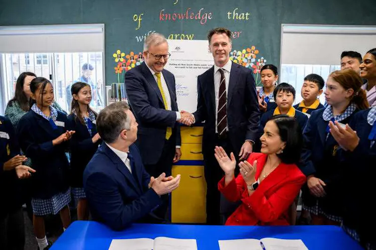 Prime Minister Anthony Albanese and NSW Premier Chris Minns shake hands in a classroom.