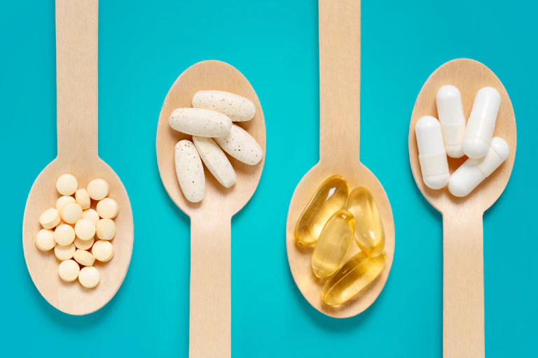 Vitamin pills and capsules on wooden spoons against aqua background