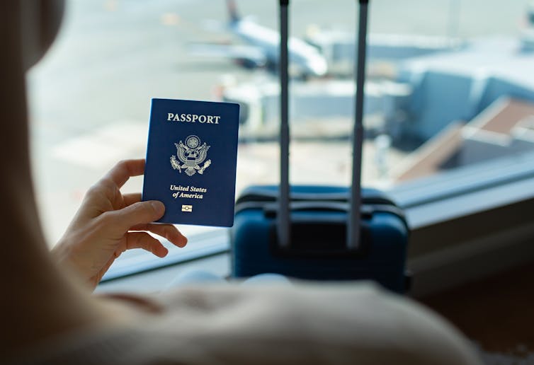 Businesswoman holding US passport and luggage while standing at airport.