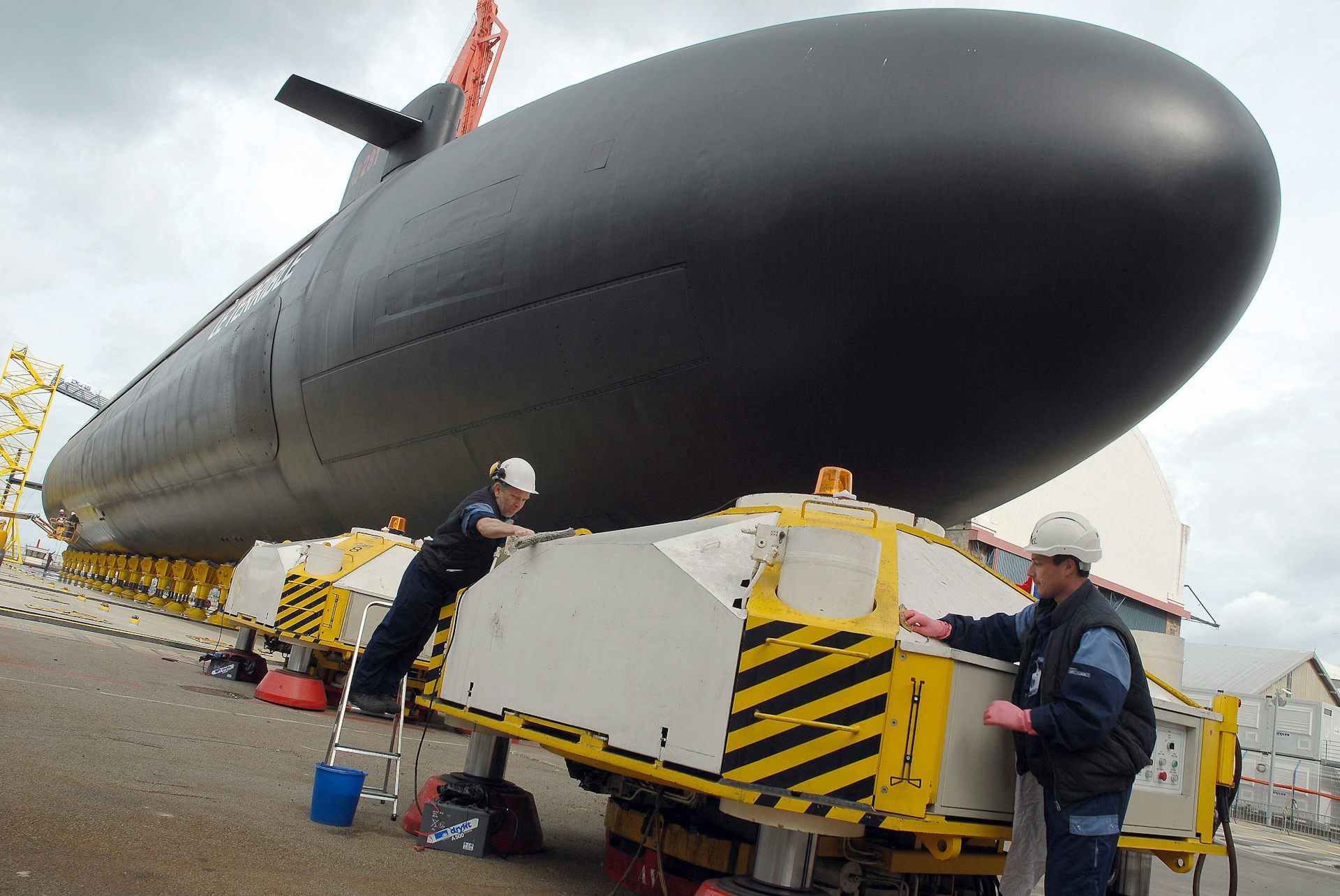 An image of a submarine at the quay and two workers in white helmets