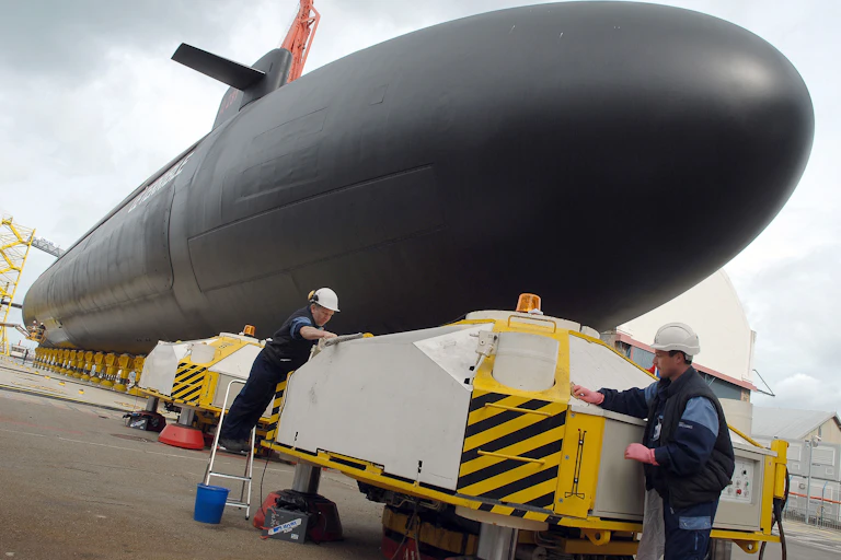 An image of a submarine at the quay and two workers in white helmets