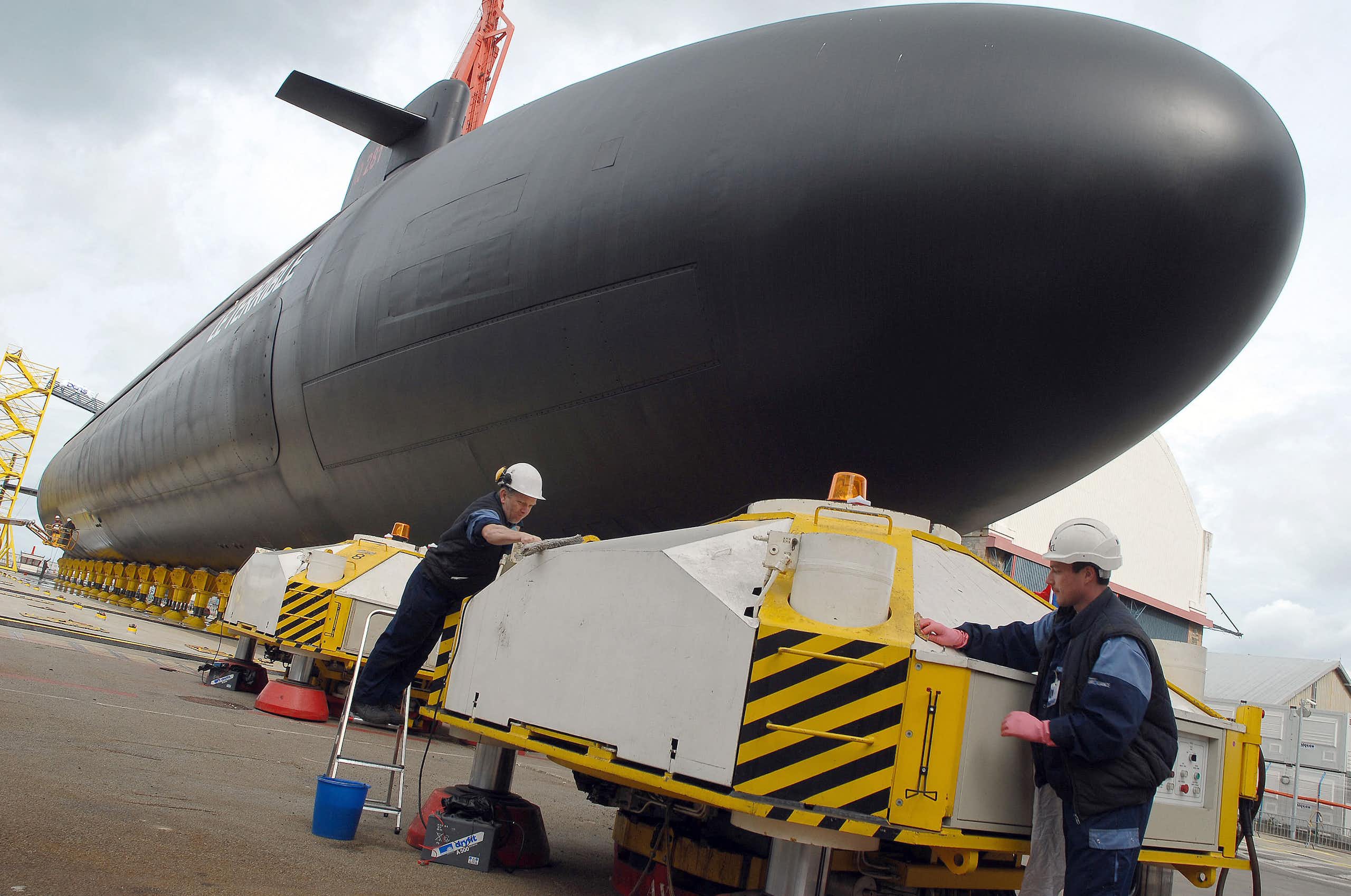 An image of a submarine at the quay and two workers in white helmets