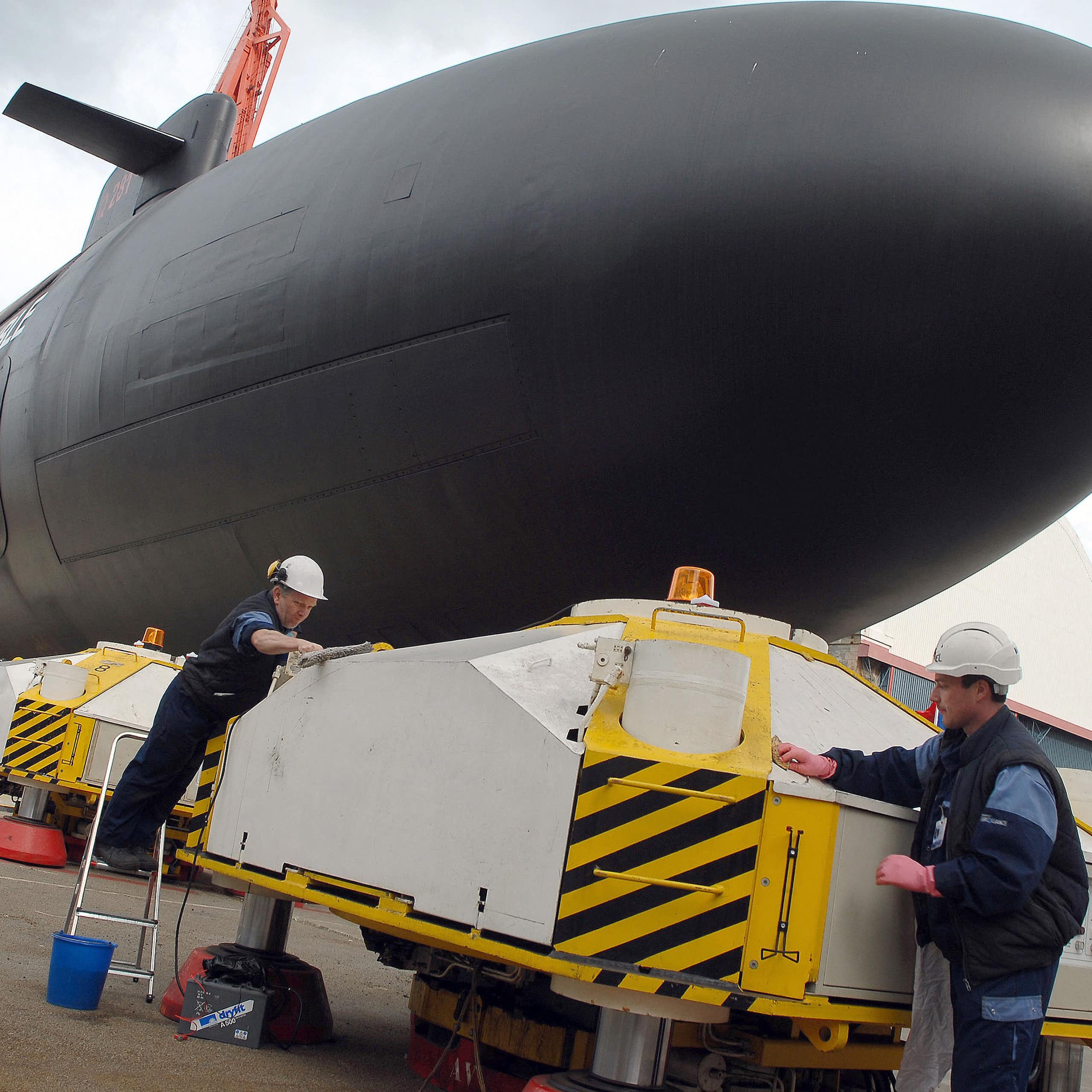 An image of a submarine at the quay and two workers in white helmets
