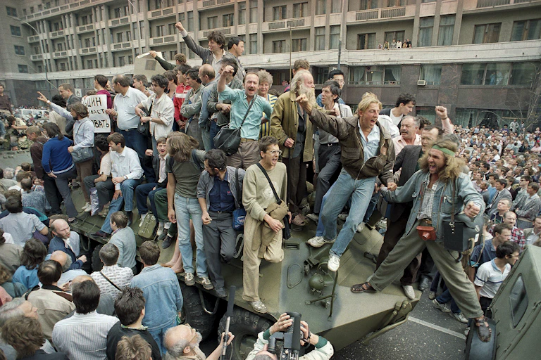 Cheering people surround and climb on a military vehicle.