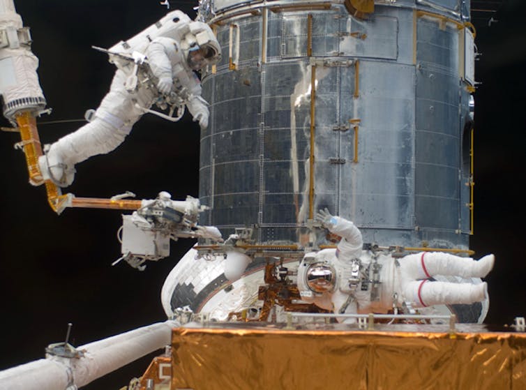 Two astronauts on an extravehicular activity in space, repairing part of a space station.