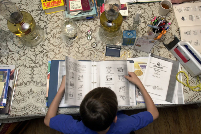 child sitting at table pages through spanish schoolwork with a variety of other objects on the table