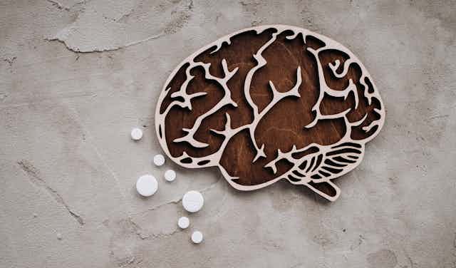 Wooden cutout of a human brain and several white tablets of different sizes