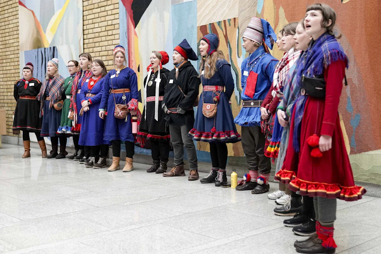 A group of activists stand in a line. They're wearing traditional Sami costumes.