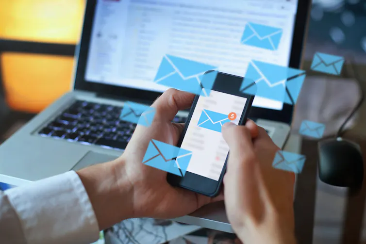 Over-the-shoulder shot of a person holding a cellphone with an unread email icon on the screen