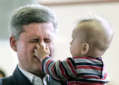 A baby grabs a grimacing grey-haired man's nose.