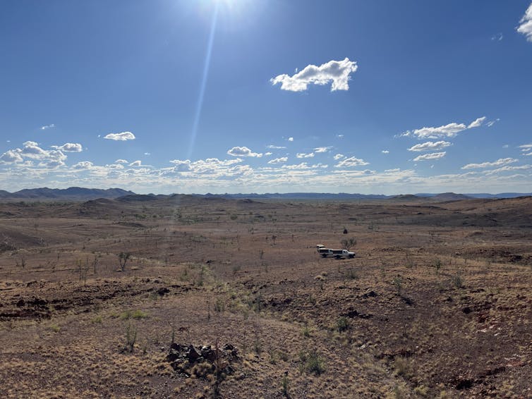 A wide view of a ruddy landscape under a blue sky with several 4WDs in the distance.
