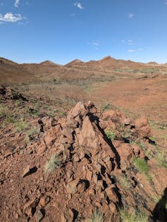 Conical red rocks in a ruddy landscape with hills in the distance.