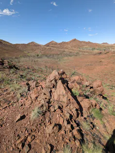 Rochas vermelhas cônicas em uma paisagem avermelhada com colinas à distância.