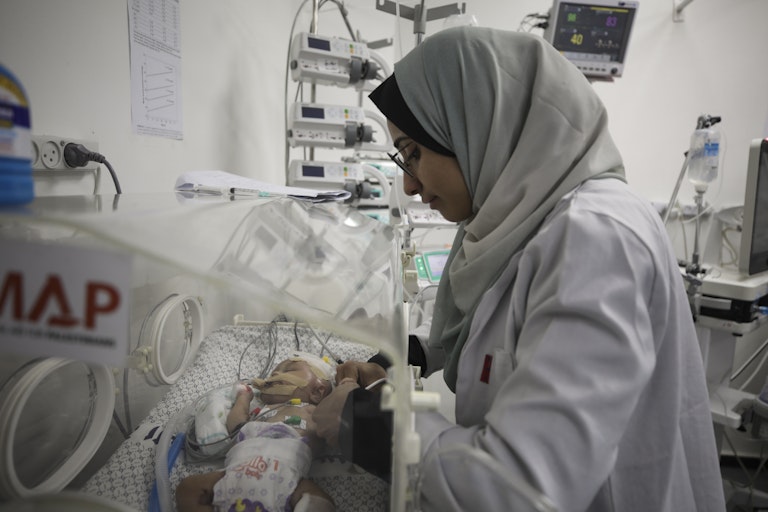 A nurse touches a baby in an incubator.