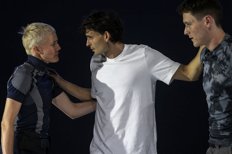 Three people on stage, Henry in a white t-shirt.