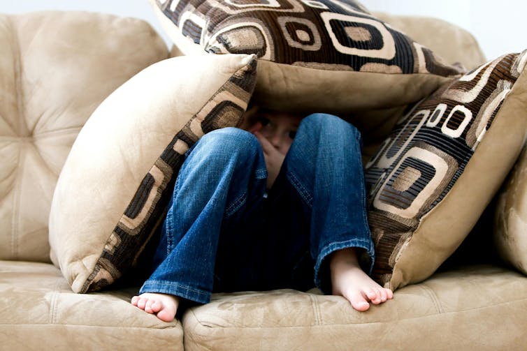 A child sits on a couch, covered in pillows