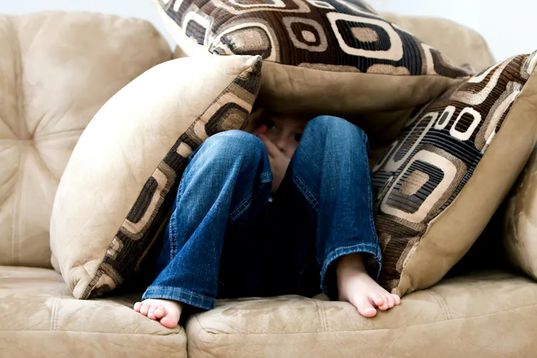 A child sits on a couch, covered in pillows