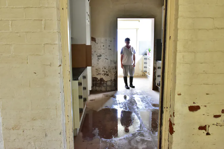 A person wearing gumboots stands inside a flooded house